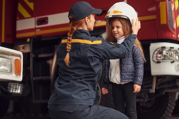 Foto indossare il casco la donna pompiere in uniforme è con una bambina