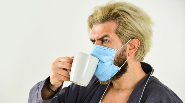 マスクを着用してコロナウイルスから保護するマスクを着用した男自宅でお茶やコーヒーを飲む検疫の概念コロナウイルスから保護する男性がフェイスマスクを着用する液滴と密接な接触によって伝染するウイルス