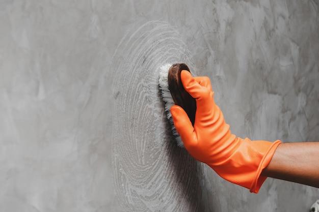 wearing orange rubber gloves is used to convert scrub cleaning on the concrete wall.