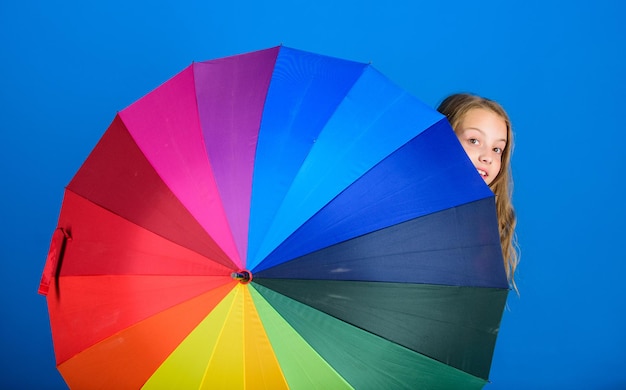 Weather forecast concept. Stay positive though rainy day. Brighten up life. Kid peek out colorful rainbow umbrella. Color your life. Girl cheerful hide behind umbrella. Colorful umbrella accessory.