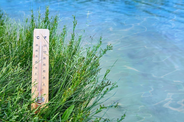 Погодный термометр в траве на фоне голубой воды