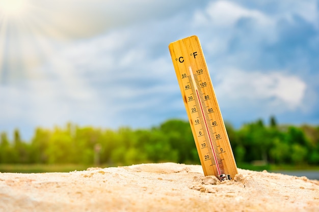 Photo weather thermometer in the sand against the sky showing a high ambient temperature