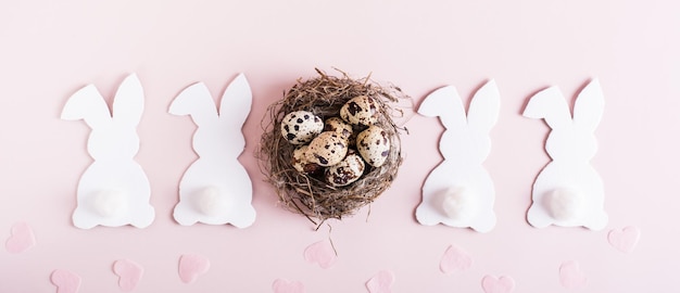 Web banner happy easter white rabbits nest with eggs and hearts on pink background top view