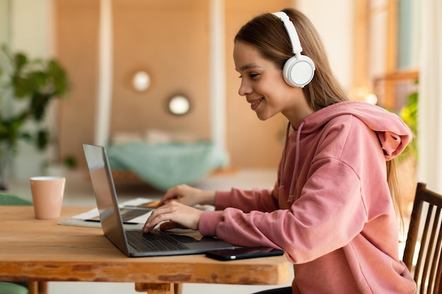 Webbased education concept Happy teenager girl in headphones having online lesson on laptop at home