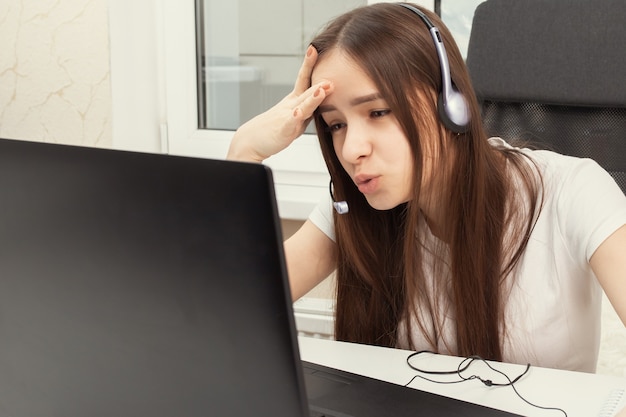 Webinar online. A student at home is studying with headphones with a microphone, trying to understand the lecture