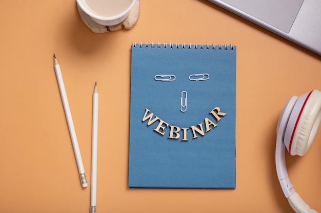 Webinartekst van houten letters op Kladblok op desktop met laptop en koffie op gekleurde achtergrond Bovenaanzicht plat lag