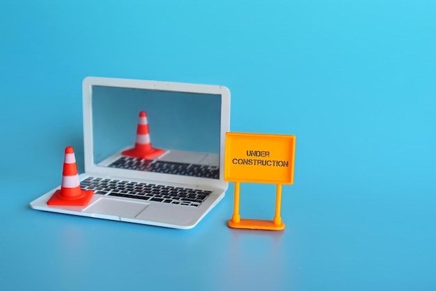 Website under construction concept laptop safety cone and\
signboard with text under construction