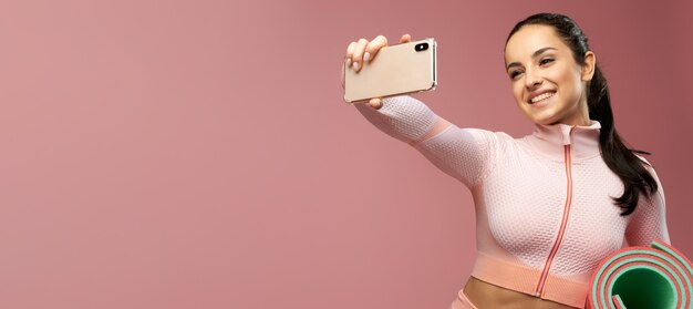 Websitekoptekst van vrolijke jonge vrouw die met yogamat selfie maakt