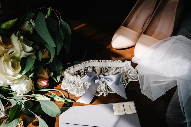 Foto accessorio di nozze sposa eleganti scarpe beige orecchini anelli d'oro fiori giarrettiera profumi sul tavolo in piedi su sfondo di legno silhouette e ombra sole lettere dalla sposa e dallo sposo