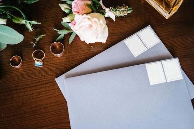 Wedding accessory bride Stylish gold rings flowers perfumes on table standing on wooden background Letters from the bride and groom flat lay top view