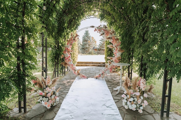 the wedding arch in the park is made of fresh flowers and dry reeds outdoor wedding ceremony in nature in a green corridor white chairs for the ceremony