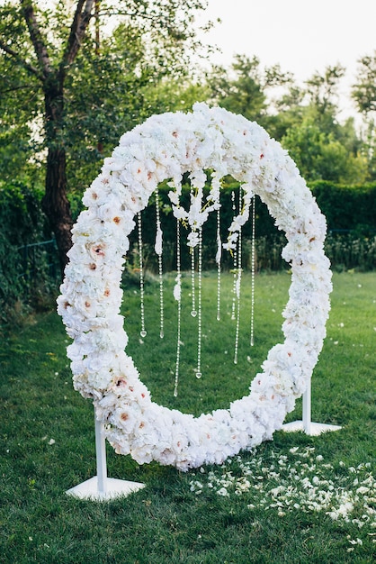 wedding arch of white flowers of a round shape decorated with beads and feathers on a background of nature