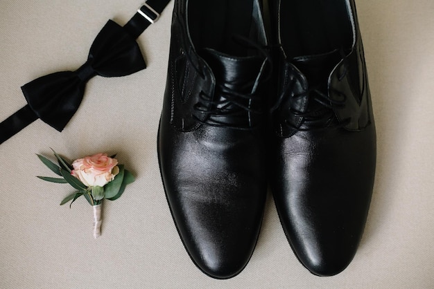 Wedding attributes a pair of leather man's shoes, black butterfly tie, boutonniere with a rose.