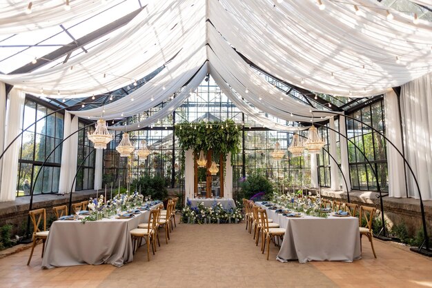 사진 온실의 결혼식 연회장은 신선한 꽃, 양초, 크리스탈 샹들리에로 장식된 테이블이 놓여 있습니다. 부드러운 선택적 초점입니다.