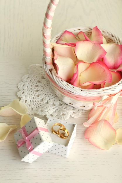 Wedding basket with roses petals and box with wedding rings on table, on light background