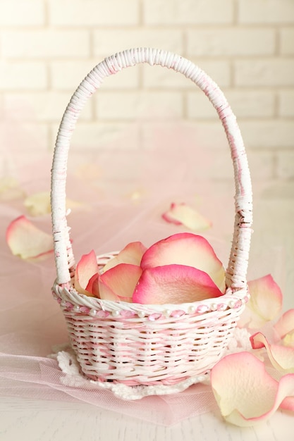 Wedding basket with roses petals on table, on light background