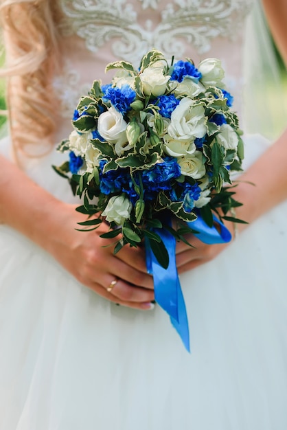 リングで花嫁の手に白いバラと青い花の美しい花束を結婚式