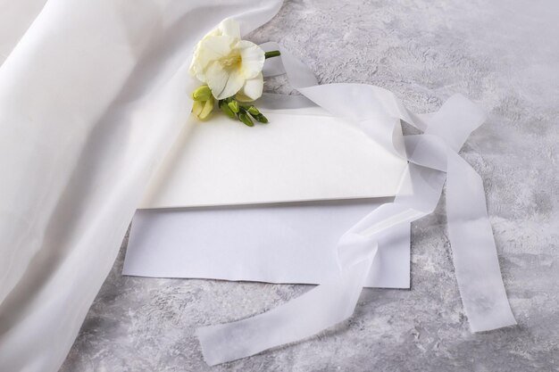 Wedding blank and an envelope with a delicate freesia flower on a light table