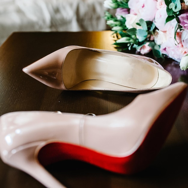 Свадебный букет невесты из розовых цветов, роз и зелени, стильные элегантные классические лакированные бежевые туфли и золотые кольца, лежащие на деревянном фоне.