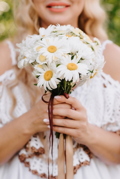 Wedding bouquet of daisies in the hands of the bride on the background of a white dress