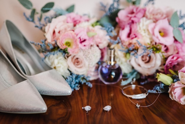 写真 ピンクの花のバラと緑の花嫁のウェディング ブーケ スタイリッシュなエレガントなクラシック シューズと 2 つの銀の結婚式のイヤリング ブレスレット クローズ アップ