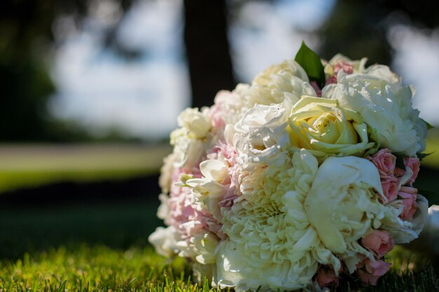 Wedding bouquet of pink and white roses, decorated with silk ribbons, lie on the green grass.