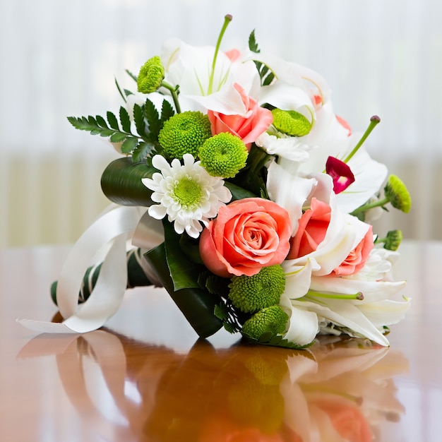 結婚披露宴で花嫁のためのバラとユリのウェディングブーケ。明るい窓を背景にテーブルの上のバラとユリのウェディングブーケ。
