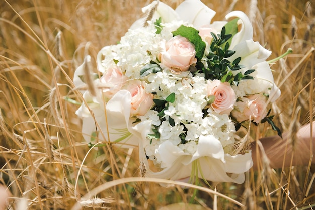 Foto bouquet da sposa in un campo di grano. anelli di nozze d'oro su un bouquet. giorno del matrimonio.