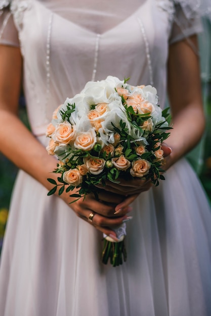 Wedding bouquet with orange roses in the hands of the bride with a ring