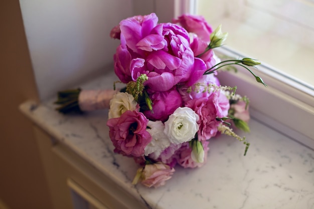 Wedding bouquet with peonies and roses lying in the window on the windowsill