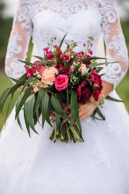 wedding bouquet with red peonies and green leaves in the hands of the bride