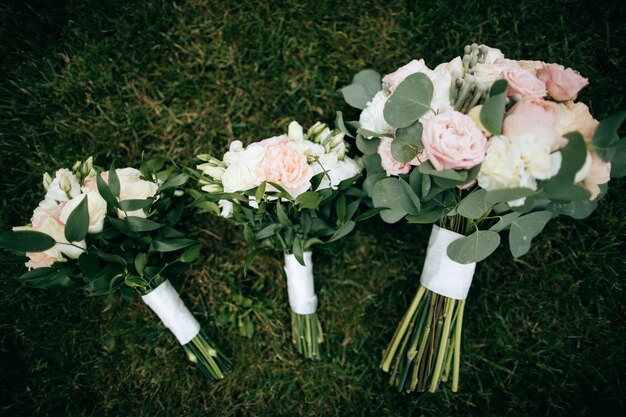 Wedding bouquets of white and pink roses lie on the green grass