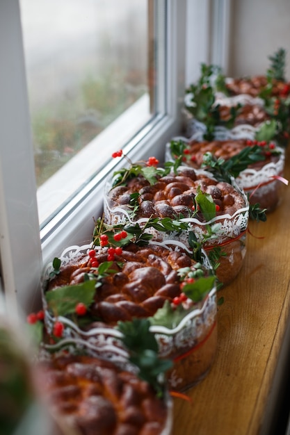 Wedding breads decorated with green leaves and berries stand on the windowsill