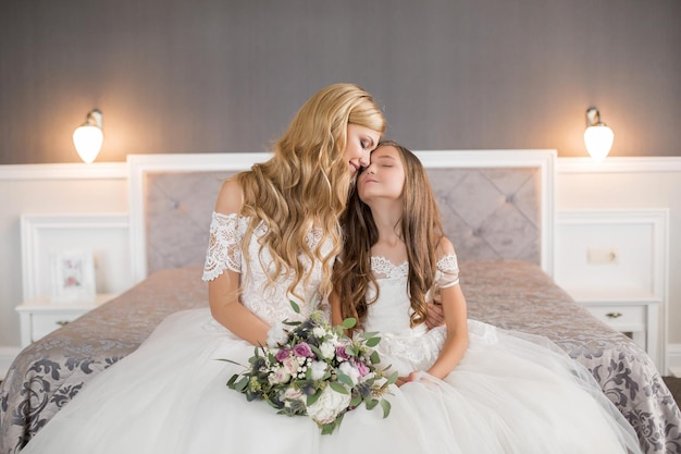 Wedding Bride in beautiful dress sitting on sofa indoors in white studio interior like at home Trendy wedding style shot in full length Young attractive caucasian brunette model like a bride