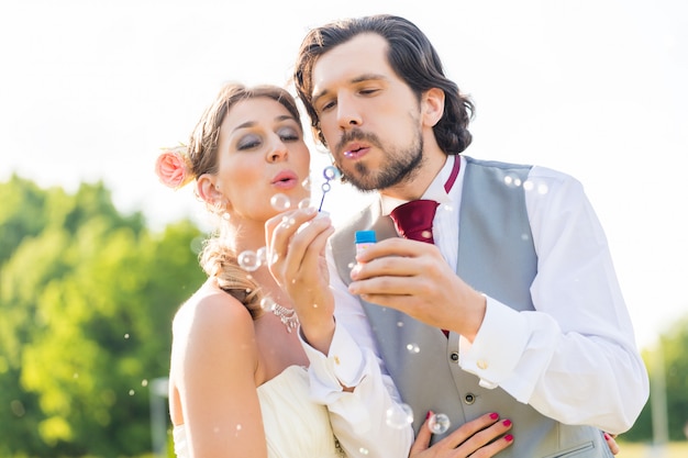 Wedding bride and groom blowing bubbles outside on field