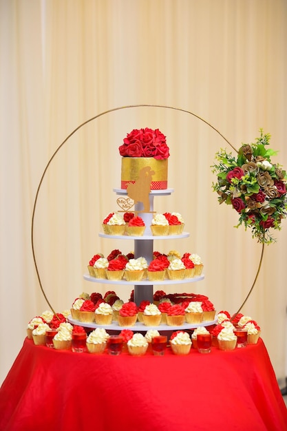 Wedding cake with red roses and cupcakes on a red tablecloth