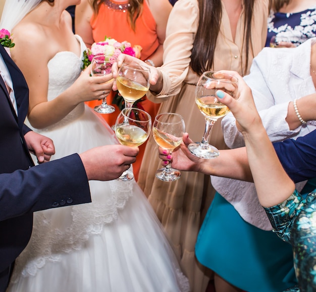 Celebrazione del matrimonio. mani che tengono i bicchieri di champagne e vino facendo un brindisi