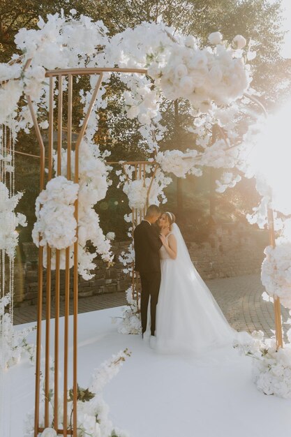Foto cerimonia matrimoniale. felice sposa, sposo e damigelle d'onore vicino al bellissimo arco di nozze