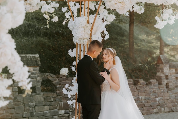 Foto cerimonia matrimoniale. felice sposa, sposo e damigelle d'onore vicino al bellissimo arco di nozze