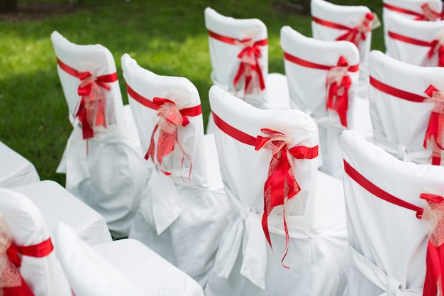 Foto cerimonia di matrimonio all'aperto con sedie bianche e nastri rossi