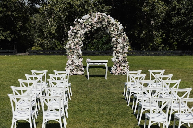 A wedding ceremony set up on a grassy lawn with white chairs and white flowers.