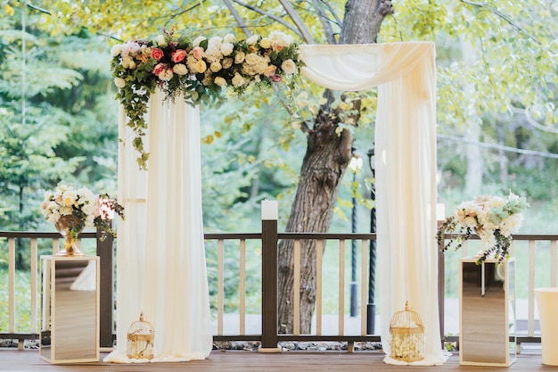 Wedding ceremony with arch decorated with pink and white flowers standing in the forest in the prese