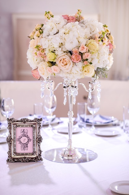 Wedding composition in the shape of a ball. peach and cream roses, white hydrangeas on a crystal chandelier, photo frame, Seating chart for guests at the event, wedding decor