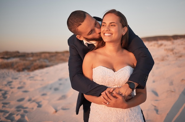 Wedding couple and beach love with a kissing bride and groom on the beach at sunset after a ceremony or celebration Happy kiss and marriage with a man and woman hugging on the sand during summer