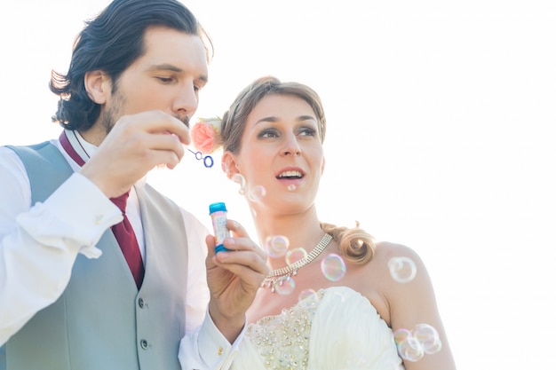 Wedding couple blowing soap bubbles outside 