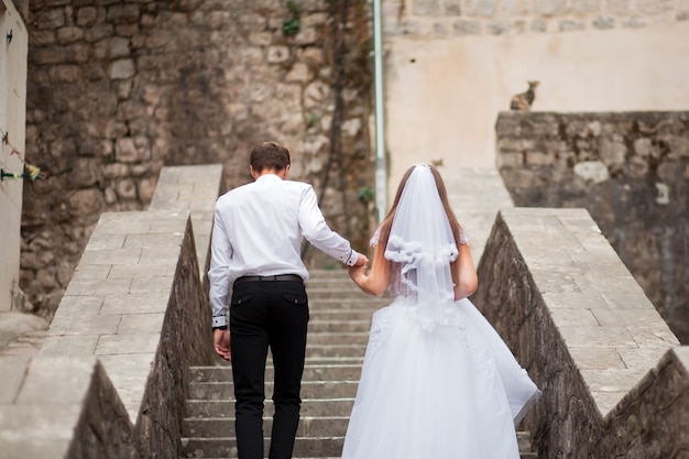 Sposi la sposa in abito e sposo a piedi lungo la strada della vecchia città tenendosi per mano