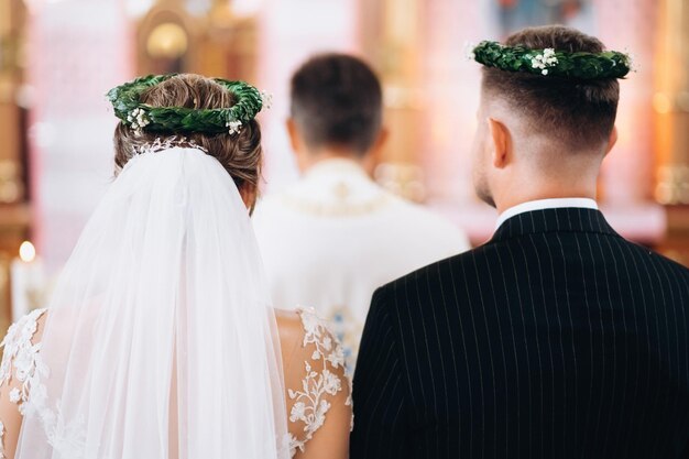 Wedding couple at church ceremony Back view of bride and groom with wreaths on his head Wedding day