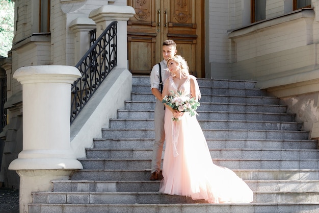 Wedding couple in city in sunny summer day. the bride and groom hugging on the stairs