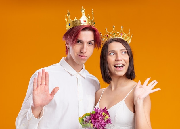 Wedding couple groom and bride with bouquet of flowers in wedding dress wearing gold crowns smiling cheerfully posing together