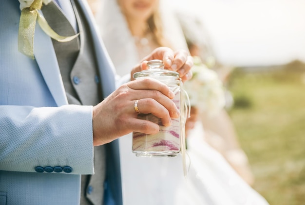 Wedding couple holding colorful sand in one glass Ceremony traditions Outdoors decorations Bride and groom in love